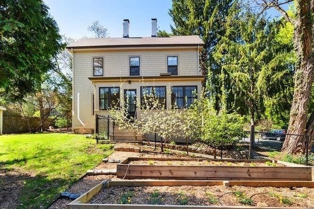 back of property featuring a lawn, fence, and a garden