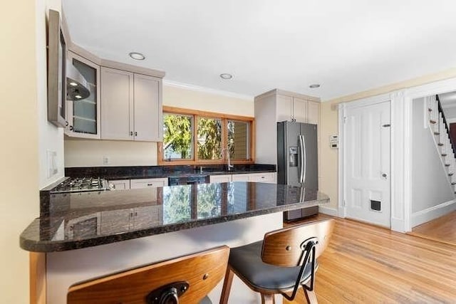 kitchen with a breakfast bar area, dark stone countertops, a peninsula, refrigerator with ice dispenser, and glass insert cabinets