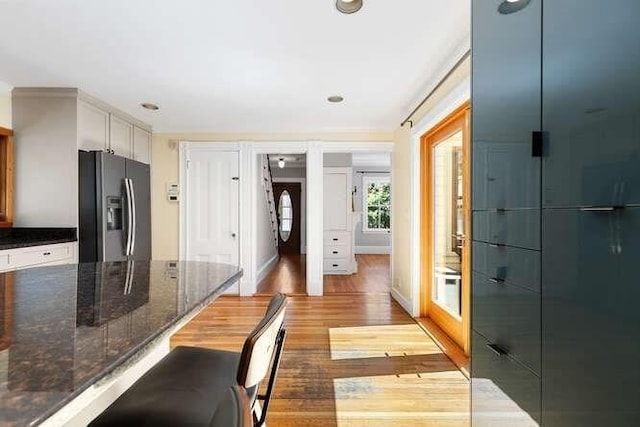 interior space with dark stone countertops, a breakfast bar area, wood finished floors, and fridge with ice dispenser