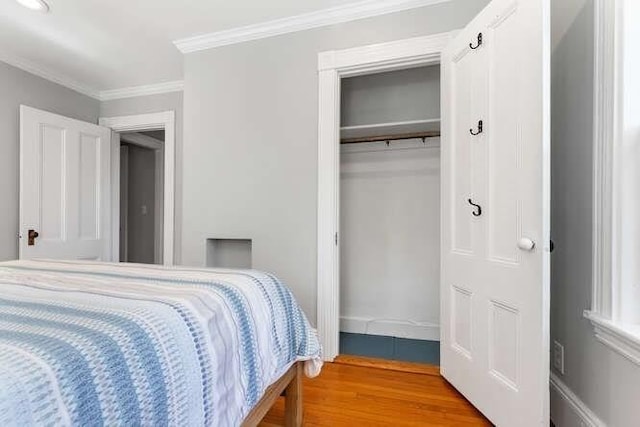 bedroom with baseboards, ornamental molding, wood finished floors, and a closet