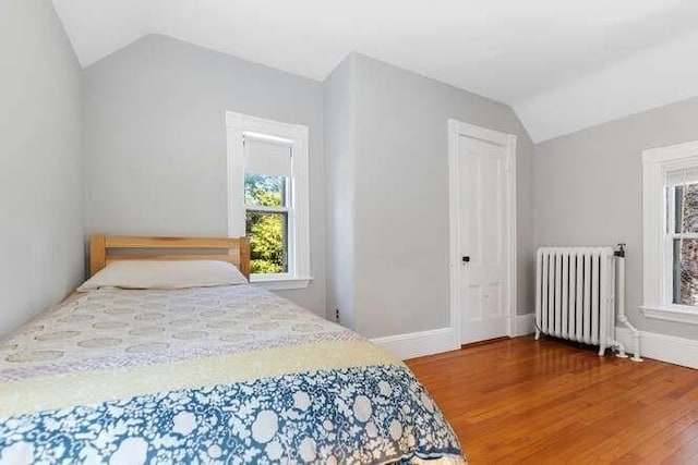 bedroom with radiator heating unit, multiple windows, wood finished floors, and lofted ceiling