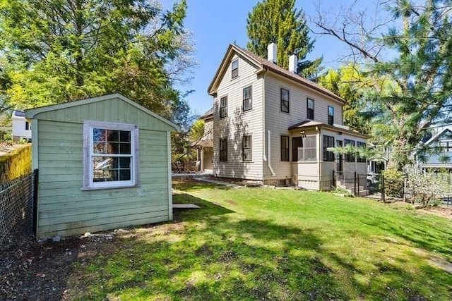 back of property with a storage unit, an outdoor structure, a lawn, and fence