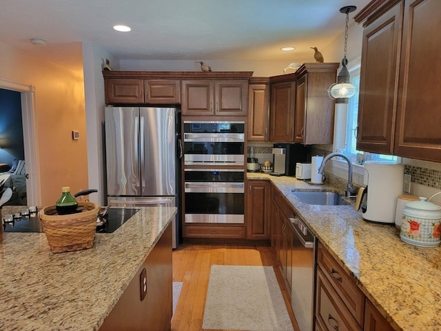 kitchen with stainless steel appliances, decorative light fixtures, decorative backsplash, sink, and light hardwood / wood-style flooring