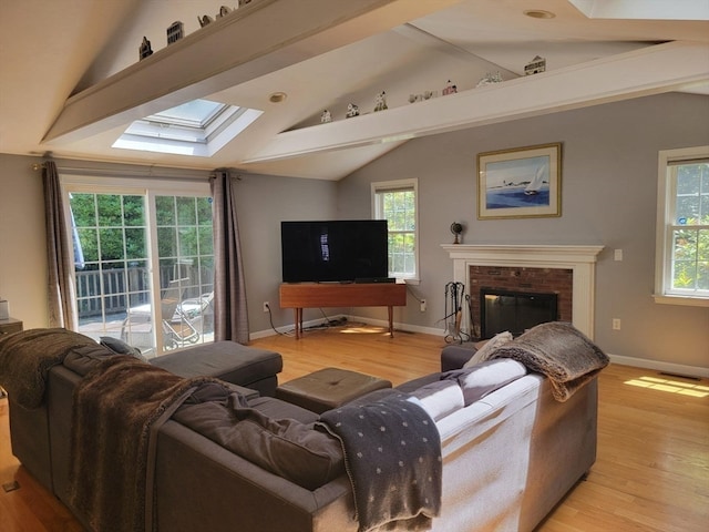 living room featuring a brick fireplace, light hardwood / wood-style floors, and vaulted ceiling with skylight