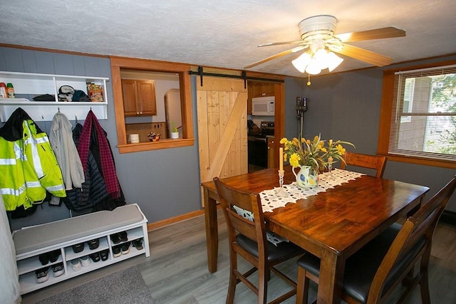 dining room featuring a barn door, wood finished floors, a ceiling fan, baseboards, and a textured ceiling