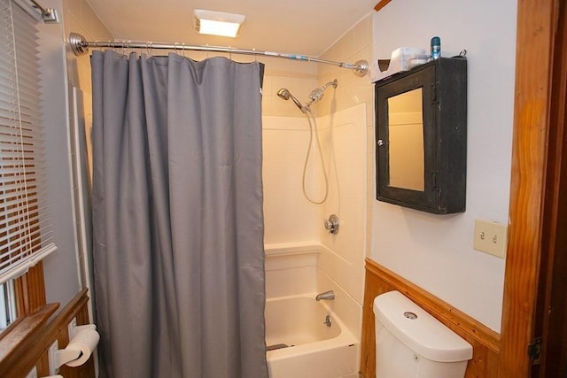 full bath featuring shower / bath combo with shower curtain, toilet, and a wainscoted wall