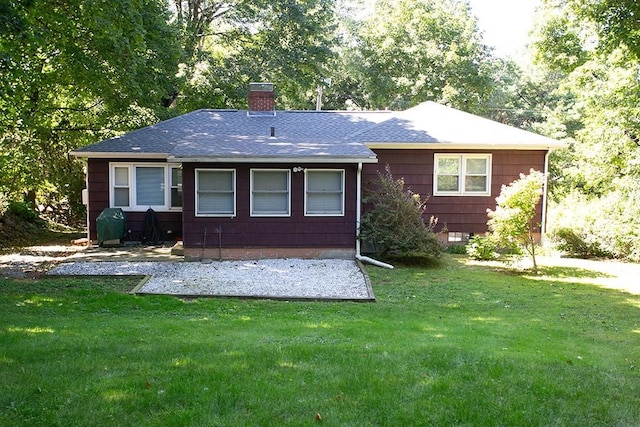 back of house featuring a chimney, a lawn, a shingled roof, and a patio