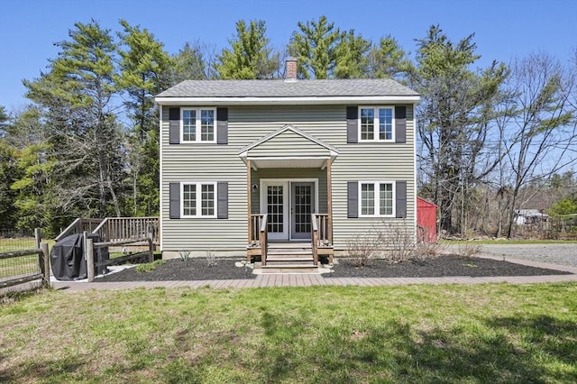 colonial-style house featuring a front lawn, fence, french doors, and a chimney