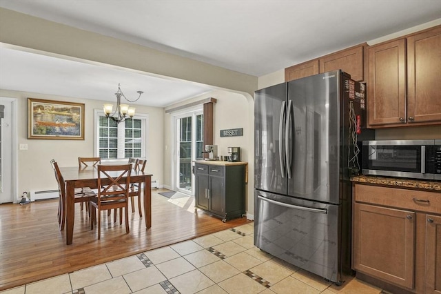 kitchen with a chandelier, brown cabinetry, light tile patterned floors, a baseboard heating unit, and appliances with stainless steel finishes