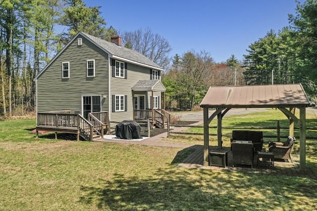 back of house featuring a wooden deck, a chimney, a lawn, roof with shingles, and a gazebo