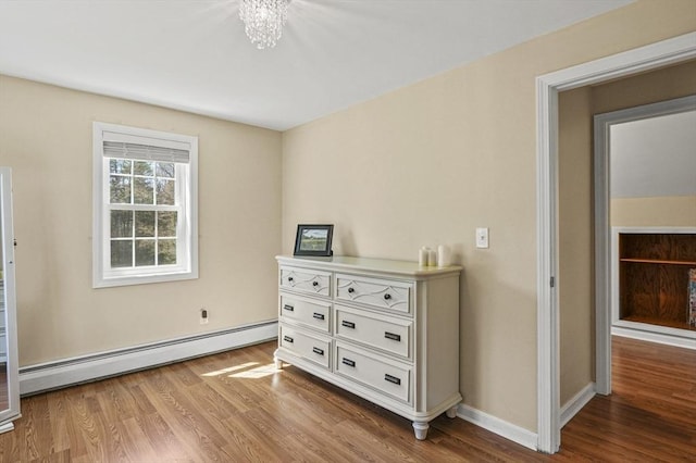bedroom featuring an inviting chandelier, wood finished floors, a baseboard heating unit, and baseboards