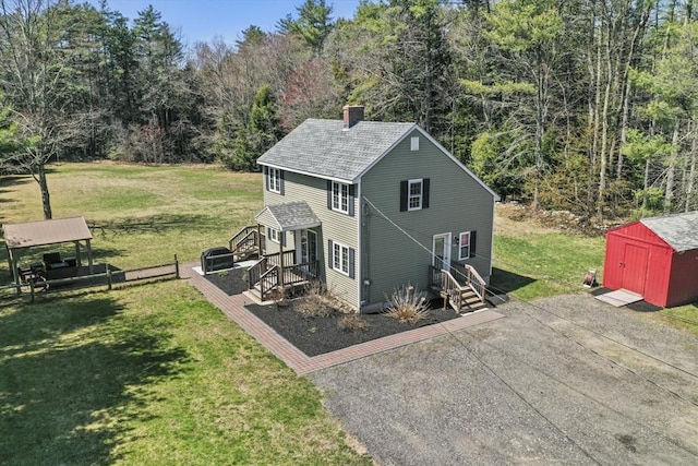 view of side of home with a chimney, an outdoor structure, a lawn, and a storage shed