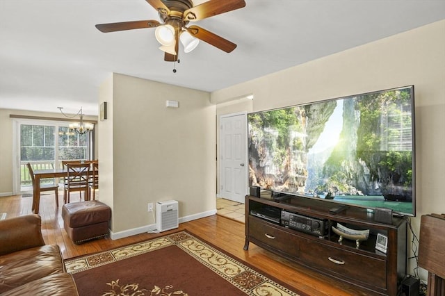 living area featuring baseboards, wood finished floors, and ceiling fan with notable chandelier