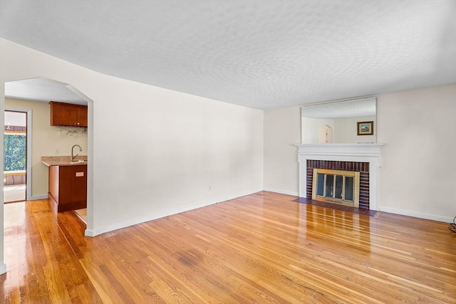 18 Fairview Rd, Westborough, MA 01581 - unfurnished living room featuring light wood-type flooring, a textured ceiling, a brick fireplace, and arched walkways