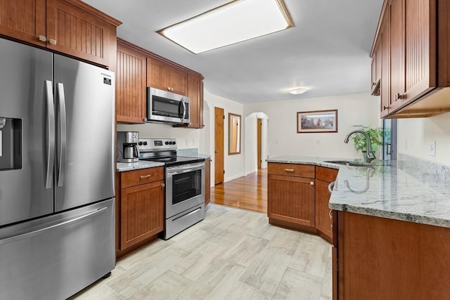 18 Fairview Rd, Westborough, MA 01581 - kitchen with stainless steel appliances, brown cabinets, arched walkways, a peninsula, and light stone counters