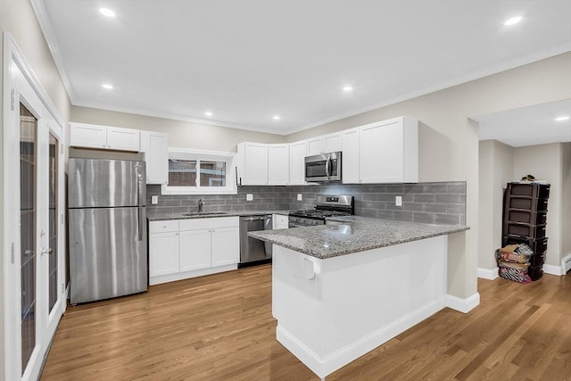 kitchen with kitchen peninsula, sink, light hardwood / wood-style flooring, appliances with stainless steel finishes, and white cabinetry