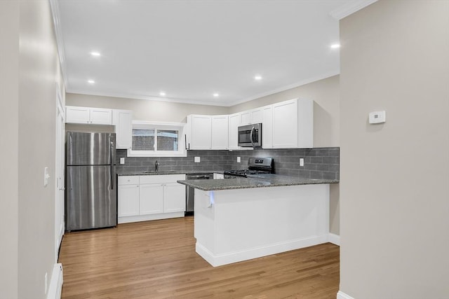 kitchen with dark stone countertops, kitchen peninsula, appliances with stainless steel finishes, and light hardwood / wood-style flooring