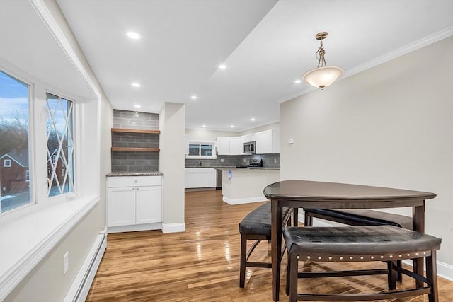 dining area with a baseboard heating unit, light wood-type flooring, and ornamental molding