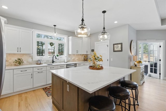 kitchen with backsplash, a center island, light wood-type flooring, stainless steel dishwasher, and a sink