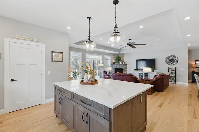 kitchen featuring a stone fireplace, light wood-style flooring, recessed lighting, a tray ceiling, and pendant lighting