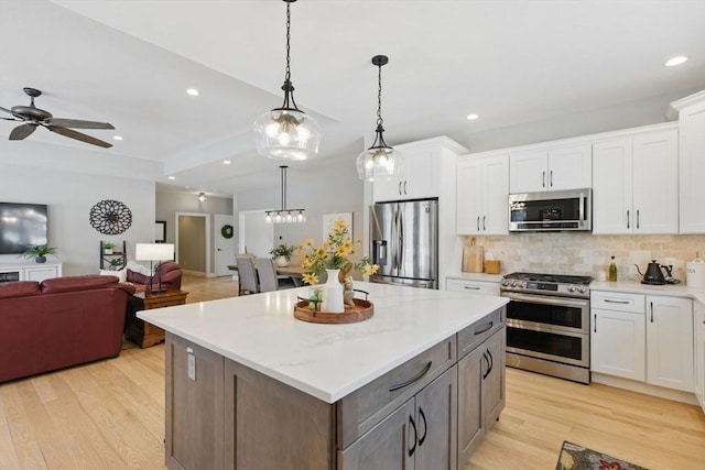 kitchen with light wood-style flooring, white cabinets, open floor plan, appliances with stainless steel finishes, and backsplash