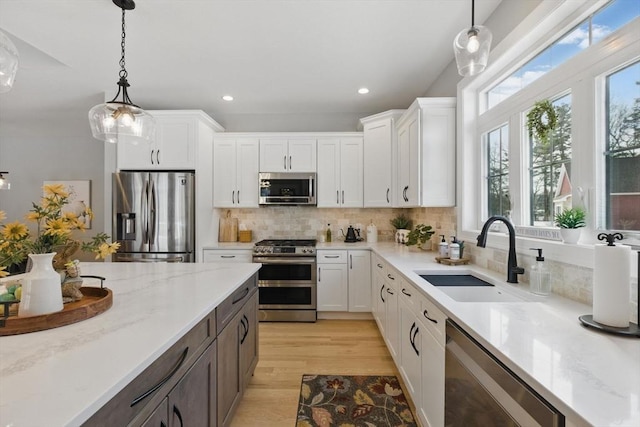 kitchen featuring hanging light fixtures, appliances with stainless steel finishes, light wood-style floors, white cabinets, and a sink