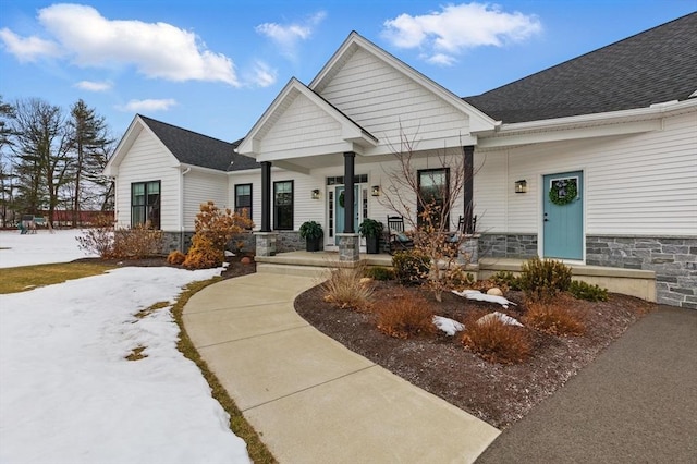 craftsman inspired home featuring a porch, stone siding, and roof with shingles