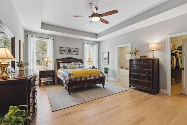 bedroom featuring a raised ceiling, baseboards, a spacious closet, and light wood finished floors