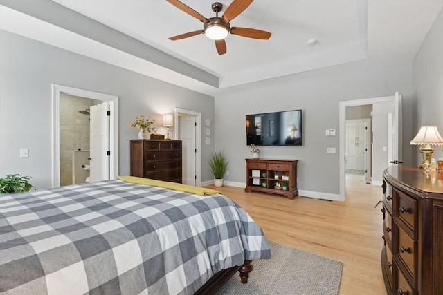 bedroom featuring ceiling fan, a tray ceiling, light wood-type flooring, and baseboards