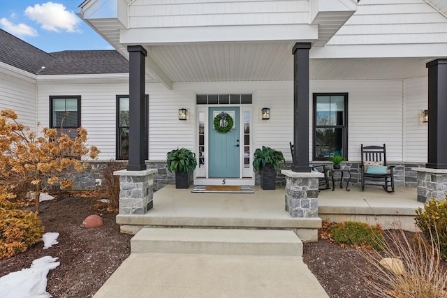 view of exterior entry featuring a porch and a shingled roof