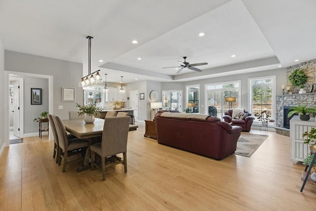 dining area with light wood-type flooring, recessed lighting, a raised ceiling, and a stone fireplace