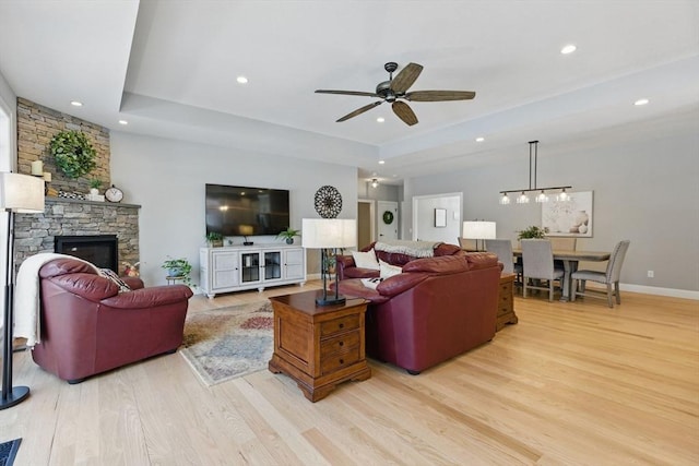 living area featuring a tray ceiling, light wood finished floors, recessed lighting, ceiling fan, and a stone fireplace