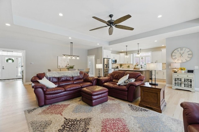 living area with light wood finished floors, baseboards, a tray ceiling, and recessed lighting