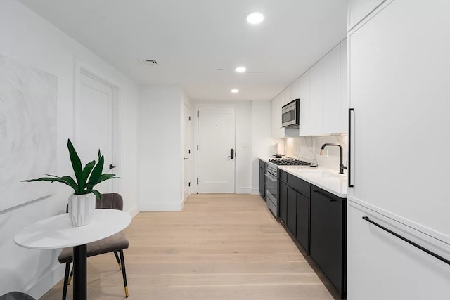 bar featuring white cabinets, stainless steel appliances, light hardwood / wood-style floors, sink, and decorative backsplash