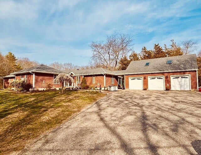 ranch-style home featuring driveway, a front lawn, central AC, and an attached garage
