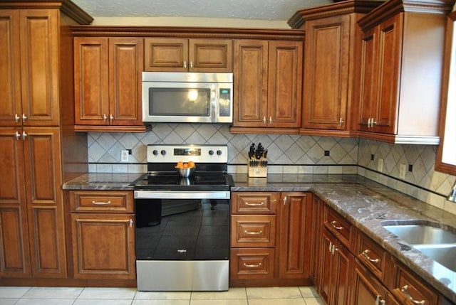 kitchen with dark stone counters, stainless steel appliances, light tile patterned flooring, and a sink