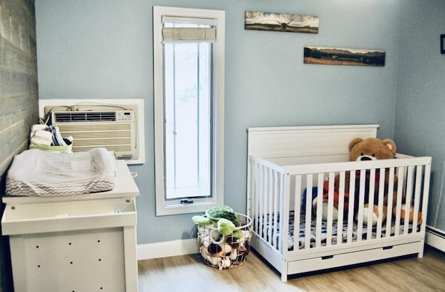 bedroom with a nursery area, wood finished floors, and baseboards