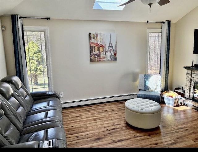 living room with a baseboard heating unit, vaulted ceiling with skylight, a ceiling fan, wood finished floors, and plenty of natural light