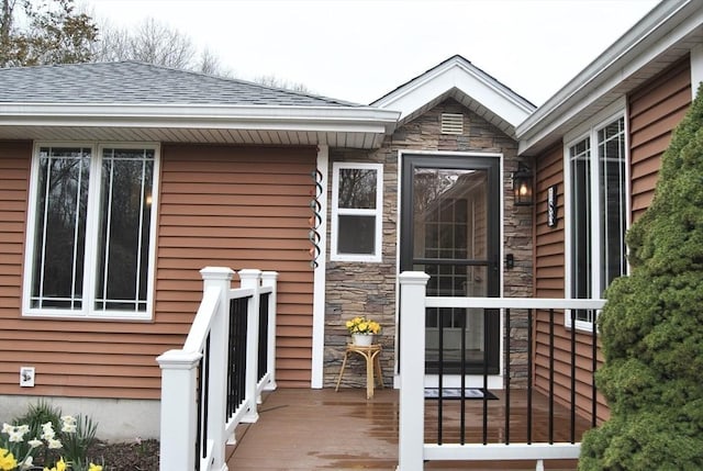 view of exterior entry with a shingled roof and stone siding
