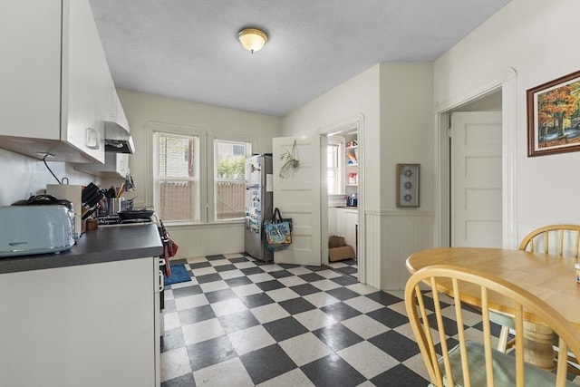 35 Ibbetson, Somerville, MA 02143 - kitchen with dark floors, white cabinets, freestanding refrigerator, wall chimney range hood, and wainscoting