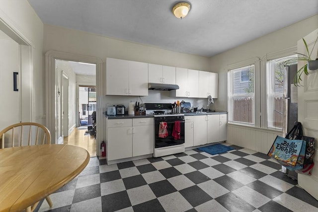 35 Ibbetson, Somerville, MA 02143 - kitchen with gas range oven, under cabinet range hood, dark countertops, dark floors, and white cabinetry