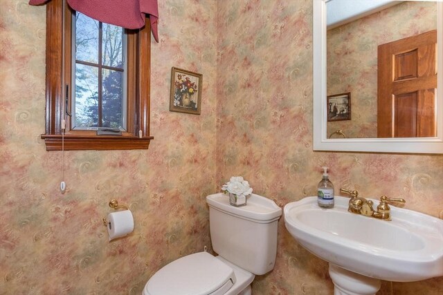 half bathroom with a sink, toilet, and wallpapered walls