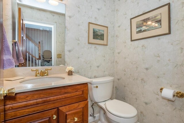 half bath featuring vanity, toilet, and wallpapered walls