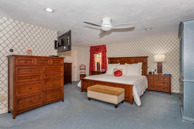 bedroom with an accent wall, light carpet, baseboards, wallpapered walls, and a ceiling fan