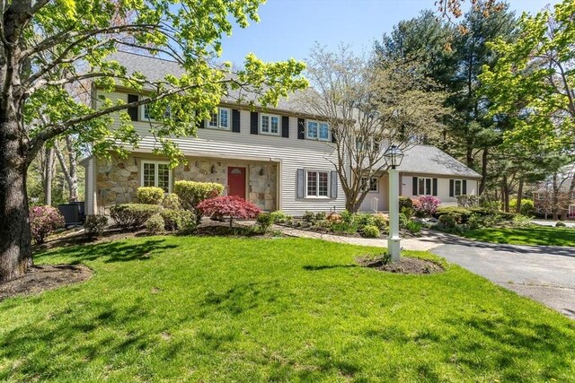view of front of home featuring cooling unit, driveway, a front lawn, and stone siding