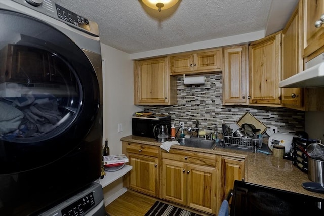 kitchen featuring sink, stacked washing maching and dryer, stove, tasteful backsplash, and a textured ceiling