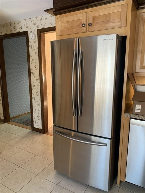 kitchen with light tile patterned floors, dark countertops, light brown cabinetry, freestanding refrigerator, and wallpapered walls