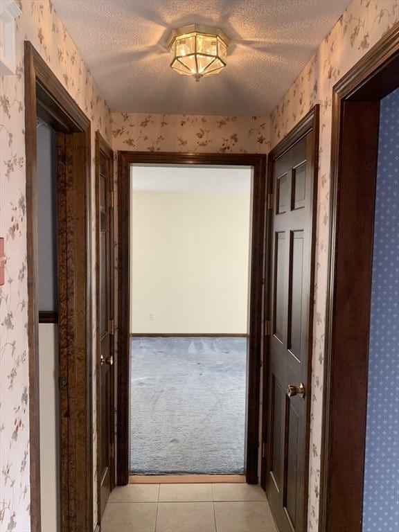 hallway with light colored carpet, light tile patterned floors, a textured ceiling, and wallpapered walls