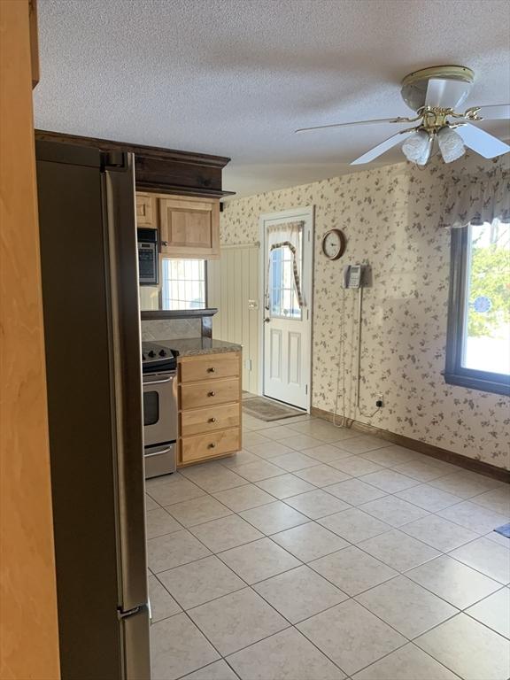 kitchen featuring a textured ceiling, light tile patterned floors, baseboards, appliances with stainless steel finishes, and wallpapered walls