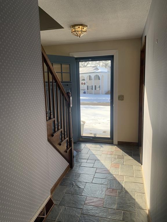 doorway to outside with a textured ceiling, baseboards, and stone tile flooring